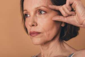 Close-up of smiling senior woman applying lifting cream, showcasing natural beauty and results of facelift or anti-aging skincare