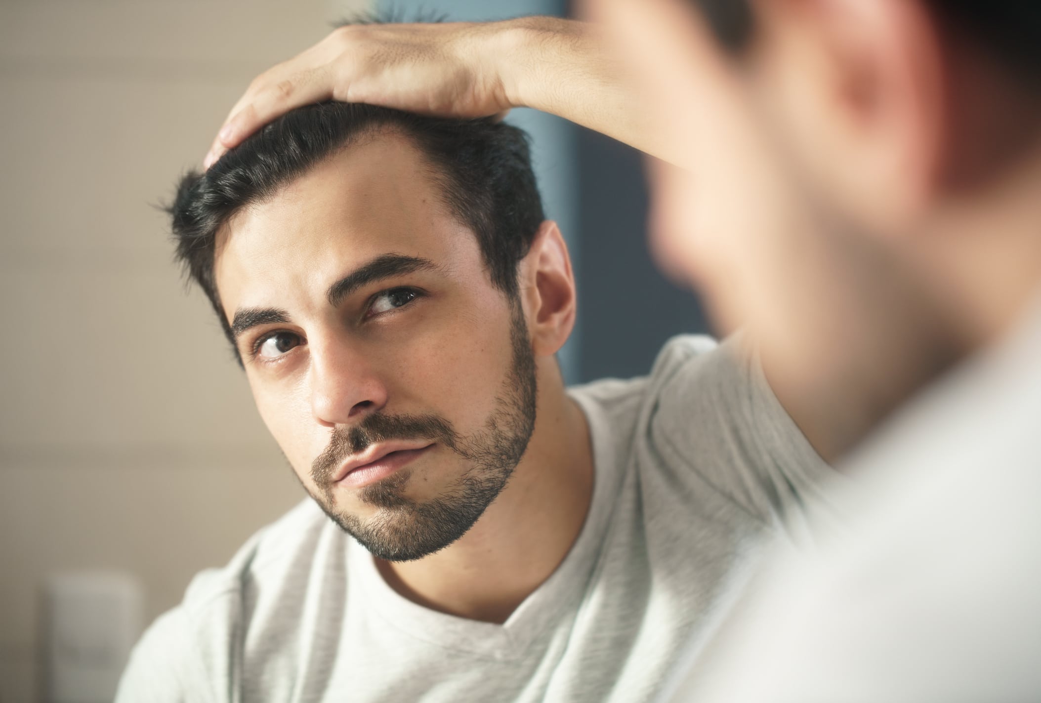 Man examines his hairline in the bathroom mirror.